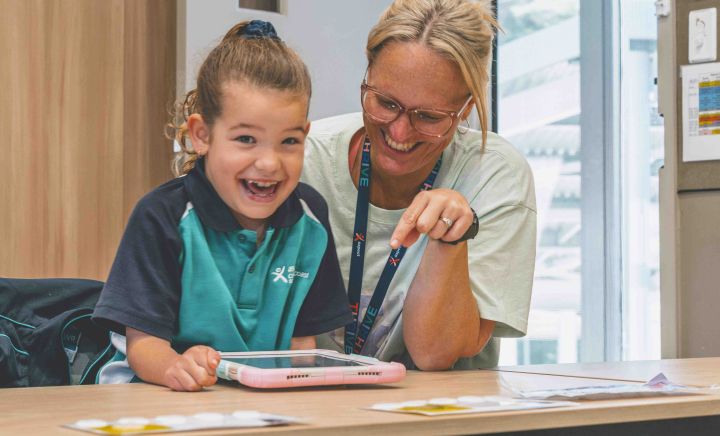 Smiling student and teacher engage with tablet learning activity